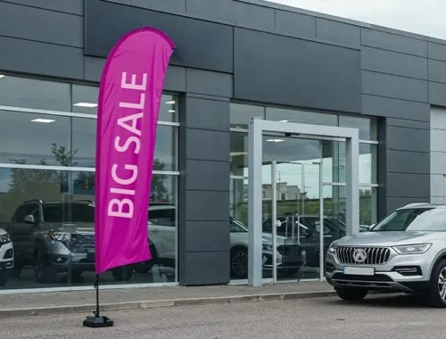Outdoor custom business flag with sale message placed at retail store entrance